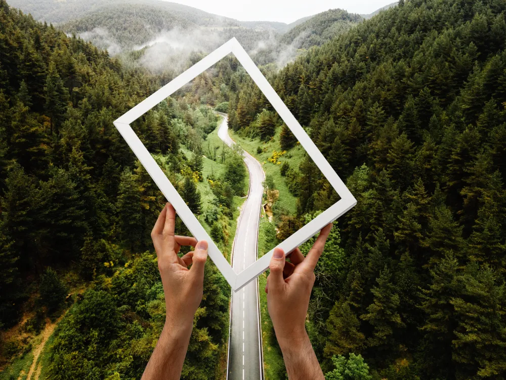 Hände halten einen Bilderrahmen vor einer Naturlandschaft